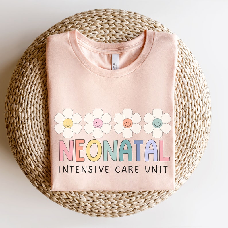 May include: A pink t-shirt with a rainbow colored word "NEONATAL" and the words "INTENSIVE CARE UNIT" in black. The word "NEONATAL" is surrounded by five white daisies with yellow centers and smiling faces.