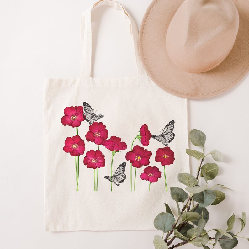 May include: A white canvas tote bag with a design of pink flowers and black butterflies. The bag has long handles.