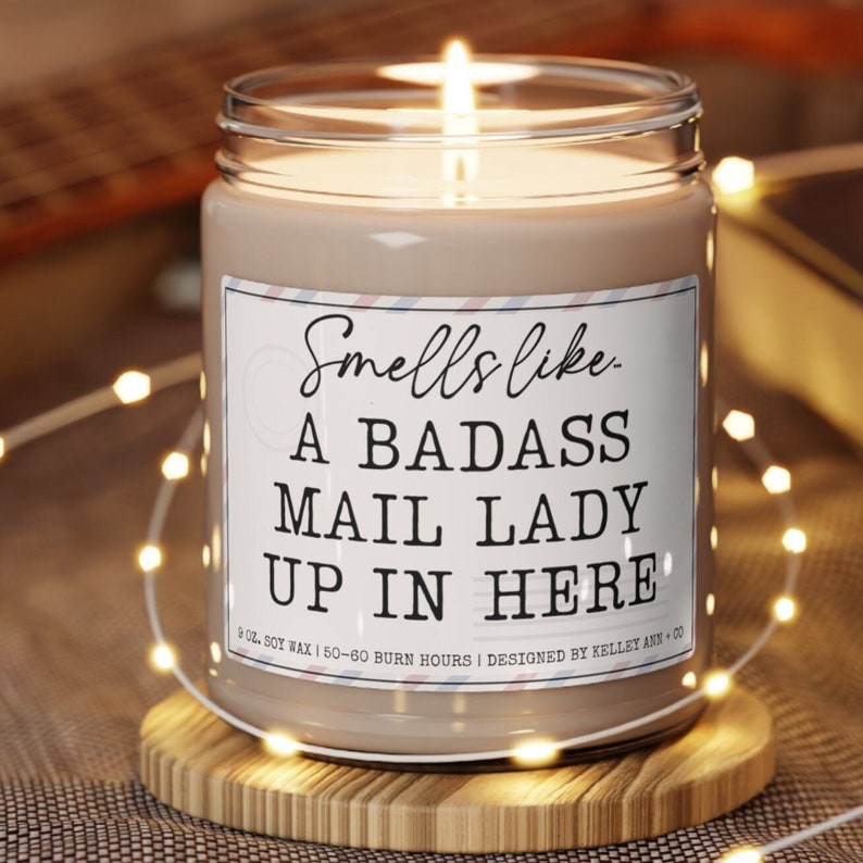 Puede incluir: Una vela de cera de soja marr&oacute;n con una etiqueta blanca que dice "Smells like a badass mail lady up in here". La vela es de 9 oz y tiene un tiempo de combusti&oacute;n de 50 a 60 horas.