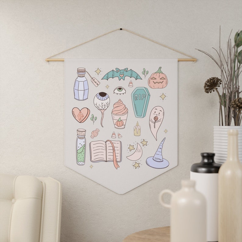 May include: A white canvas wall hanging with a variety of Halloween-themed illustrations, including a bat, a pumpkin, a ghost, a witch's hat, an eye, a coffin, a heart, a potion bottle, a book, a crescent moon, and a candy cane.