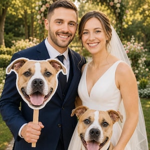 May include: A custom dog face cutout on a wooden stick featuring a tan and white pit bull mix with a happy expression, held next to a tan and white pit bull wearing a black bow tie collar, standing beside a couple in formal wedding attire.