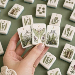 May include: A set of rectangular white tiles with rounded corners, each featuring botanical illustrations and numbers. The designs include a greenhouse, a moth, a terrarium, and various ferns. The tiles have a light blue base edge.