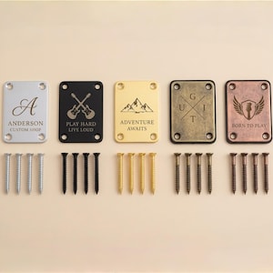 Puede incluir: Un conjunto de placas para mástil de guitarra en plata, negro, dorado, bronce y latón envejecido. Cada placa presenta diseños y textos únicos, incluyendo una inicial en cursiva y las palabras "Adventure Awaits".