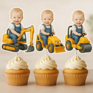 Puede incluir: Tres cupcakes cubiertos con glaseado blanco y chispas doradas. Cada cupcake tiene un adorno decorativo con un bebé sonriente con overoles azules conduciendo un vehículo de construcción amarillo: una excavadora, un tractor y un rodillo. Los cupcakes están sobre una superficie clara.