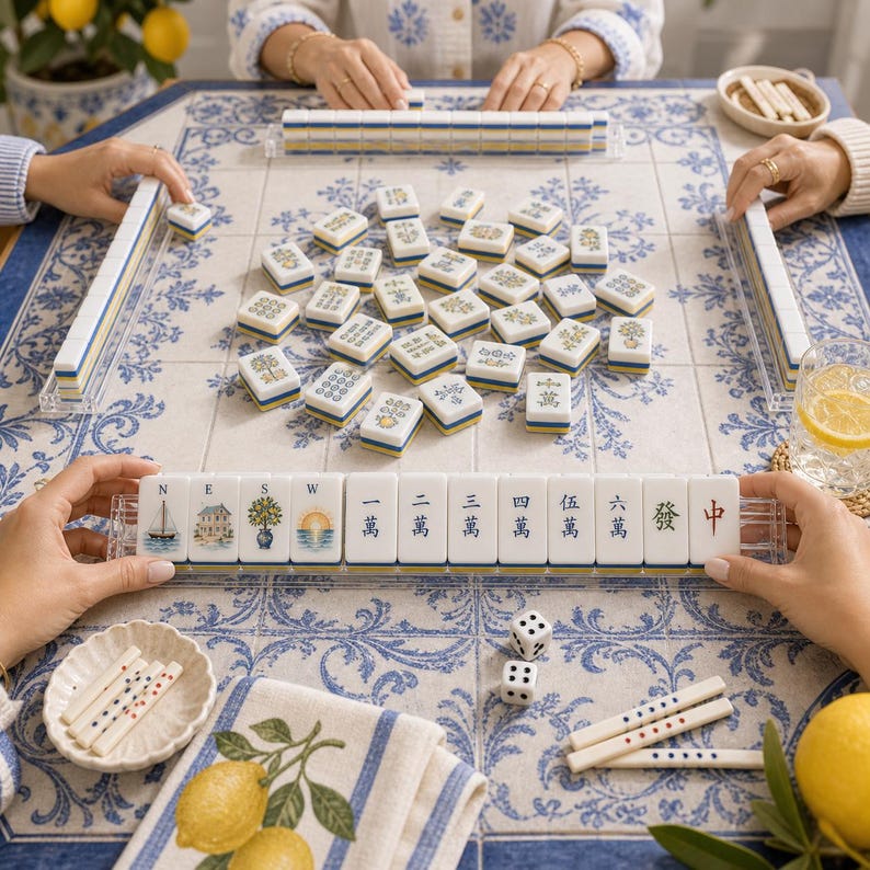 May include: A Mahjong set featuring white tiles with blue and yellow accents, including illustrations of a sailboat, house, tree, and sun, alongside Chinese characters. The set includes a tile rack, two white dice, and scoring sticks on a blue and white patterned surface.