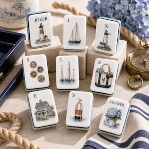 May include: A set of rectangular white tiles with nautical illustrations, including a lighthouse labeled JOKER, a sailboat labeled 1, a lighthouse labeled N, four compasses labeled 5, sailboats labeled 3, a tote bag labeled 8, a house labeled E, a buoy labeled S, and hydrangeas labeled FLOWER.