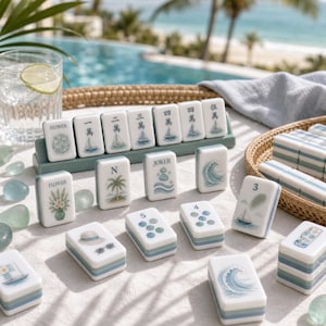May include: A set of white mahjong tiles featuring blue and green illustrations of sailboats, palm trees, ocean waves, flowers, and hats. Some tiles display Chinese characters and the word JOKER. The tiles are arranged on a green rack and a tray.