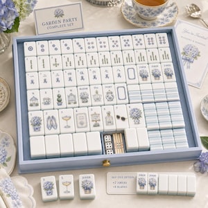 Puede incluir: Un juego de mahjong completo en una bandeja de madera azul claro con fichas blancas que presentan caracteres en tinta azul e ilustraciones florales. El set incluye fichas numeradas, de vientos y comodines decorados con motivos de hortensias.