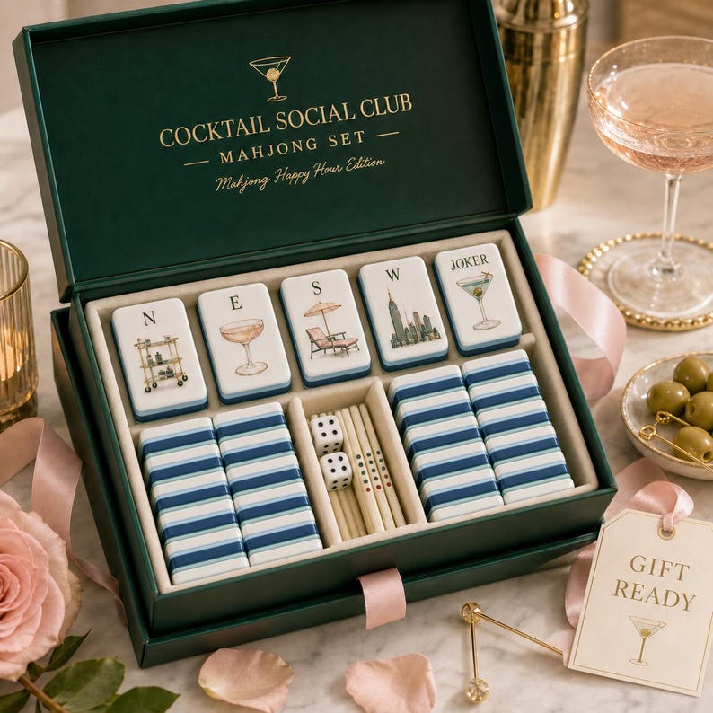 K&ouml;nnte beinhalten: Ein dunkelgr&uuml;ner Mahjong-Set-Kasten mit goldenem Schriftzug COCKTAIL SOCIAL CLUB MAHJONG SET. Im Inneren befinden sich wei&szlig;e Spielsteine mit Abbildungen eines Barwagens, Cocktails, Liegestuhls, einer Skyline und eines Martinis sowie blaue Streifensteine.