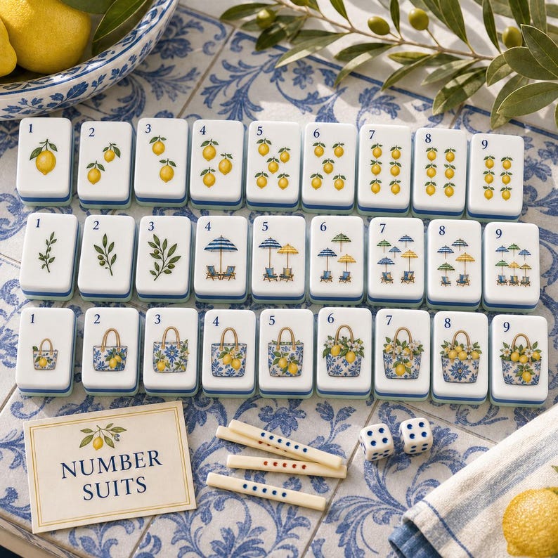 May include: A mahjong tile set featuring three rows of nine white tiles with blue and green illustrations of lemons, beach umbrellas, and floral tote bags. The set includes a card labeled NUMBER SUITS, three small counting sticks, and two dice.