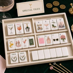 K&ouml;nnte beinhalten: Ein mit beigem Samt ausgekleidetes Tablett mit wei&szlig;en Mahjong-Steinen, die bunte Illustrationen von Cocktails, Modeartikeln und Stadtszenen zeigen. Die Steine sind in Abschnitte unterteilt, die als Dragons, Winds, Flowers, Jokers und Blanks beschriftet sind. Ein Schild tr&auml;gt die Aufschrift SPECIAL TILES.