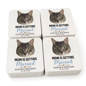 以下が含まれることがあります： グレーのトラ猫の顔と、黒と青で「MOM IS GETTING Married」の文字が入った正方形の白いコースター。 「SARAH & MICHAEL」の名前と日付「09.15.2024」もコースターに印刷されています。 コースターは積み重ねられています。