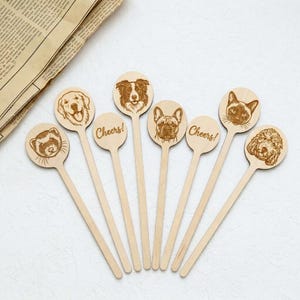 Può includere: Una collezione di bastoncini di legno per mescolare bevande con ritratti di animali incisi, tra cui un cane, un gatto e un furetto. Alcuni bastoncini hanno la scritta "Cheers!". I bastoncini sono in legno chiaro.