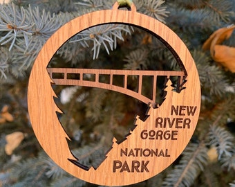 May include: Wooden ornament featuring a silhouette of a bridge and trees with the text "New River Gorge National Park".
