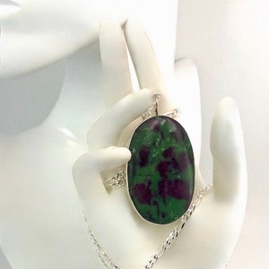 May include: A silver chain necklace with a large oval pendant featuring a green and purple gemstone. The pendant is set in silver and has a polished finish.