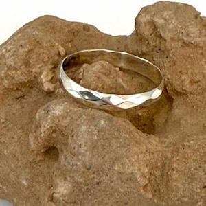 May include: A silver hammered band ring, shown on a brown rock background.