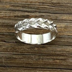 Puede incluir: Un anillo de banda de plata con un diseño trenzado.