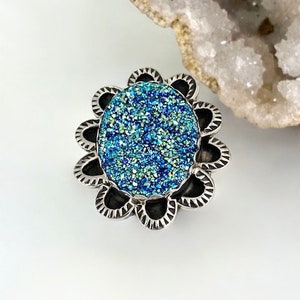 May include: A silver ring with a blue and green sparkly stone set in a flower-shaped design.