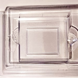 Könnte beinhalten: Eine quadratische Box aus klarem Kunststoff mit einer kleineren quadratischen Box im Inneren. Die Box ist für die Aufbewahrung eines kleinen Gegenstands wie Schmuck oder eines kleinen Schnickschnacks konzipiert.