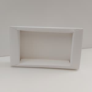 May include: A white cardboard box with a rectangular opening. The box is folded and ready to be assembled.