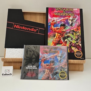 以下が含まれることがあります： ウィザード＆ウォリアーズのゲームカートリッジとゲームボックス。ボックスは黒地に赤文字、カートリッジは黒地に剣を持った戦士が描かれたカラフルなラベルです。