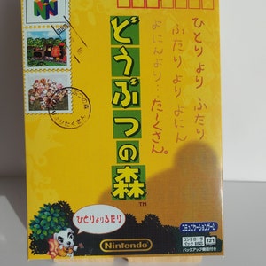 Puede incluir: Una caja de juego amarilla de Nintendo 64 con una imagen de un perro tocando el ukelele. El juego se llama "Animal Crossing" y el texto en la caja dice "¡Más diversión con amigos!"
