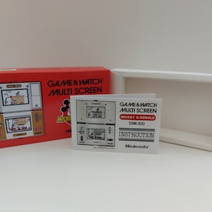 Può includere: Una scatola rossa con una console di gioco portatile Game & Watch Multi Screen Mickey & Donald (DM-53) bianca. La scatola ha un'immagine della console e il testo "GAME & WATCH MULTI SCREEN" e "MICKEY & DONALD". C'è anche un foglio di istruzioni separato con il testo "GAME & WATCH MULTI SCREEN MICKEY & DONALD (DM-53) INSTRUCTION Nintendo".