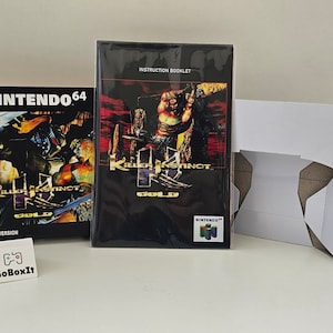 Op de afbeelding: Een Nintendo 64-spelcartridge en een instructieboekje voor Killer Instinct Gold. De speldoos is zwart met gouden accenten en toont een personage uit het spel. Het instructieboekje is zwart met een rode achtergrond en toont een personage uit het spel.