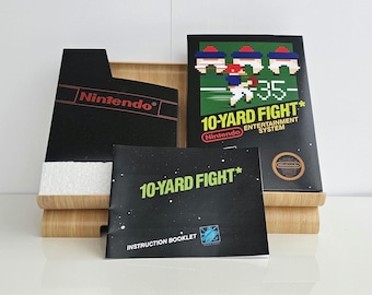 May include: A Nintendo Entertainment System game cartridge, instruction booklet, and game box for the game "10-Yard Fight". The game box is black with red and white text and features a pixelated image of football players. The instruction booklet is black with white text and a blue and white logo.