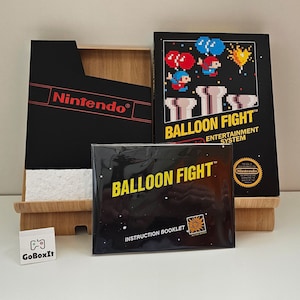 Puede incluir: Un cartucho de juego negro de Nintendo Entertainment System con un folleto de instrucciones negro. El cartucho de juego está etiquetado como "Balloon Fight" y el folleto de instrucciones está etiquetado como "Balloon Fight" con el texto "Instruction Booklet".