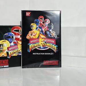 以下が含まれることがあります： Mighty Morphin Power Rangersのスーパーファミコンゲームカートリッジ。ゲームカートリッジは黒地に赤、青、黄色のカラーリング。カートリッジの前面には、象徴的なコスチュームを着たパワーレンジャーのグループが描かれている。テキスト「Mighty Morphin Power Rangers」は黒地に白で印刷されている。テキスト「Super Nintendo Entertainment System」は黒地に白で印刷されている。テキスト「PAL Version」は黒地に白で印刷されている。