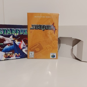 Op de afbeelding: Een Nintendo 64-spelboxset voor Star Fox 64. De doos is wit met een uitsparing voor de gamecartridge. De gamecartridge zit in een doorzichtige plastic behuizing met een geel en oranje label met de tekst "Star Fox 64". De instructiehandleiding is ook inbegrepen. De game bevat een Rumble Pak-controlleraccessoire.