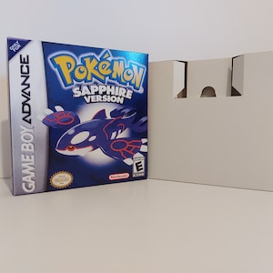 Może przedstawiać: Niebieskie pudełko gry Game Boy Advance z tytułem "Pokémon Safir Wersja" i obrazkiem niebieskiego i czerwonego Pokemona na przodzie. Pudełko znajduje się obok białego kartonu.