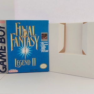 以下が含まれることがあります： 青い背景と金色の文字が入った、Final Fantasy Legend II Game Boyゲームボックス。ボックスの隣には白い段ボールのインサートがあります。ゲームボックスには任天堂とスクウェアのロゴがあります。