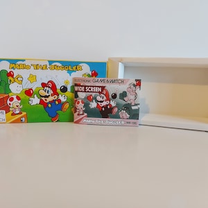 May include: A vintage Game & Watch handheld game console featuring Mario the Juggler. The box is yellow with a red and green image of Mario juggling hearts. The game cartridge is red and features a wide screen.
