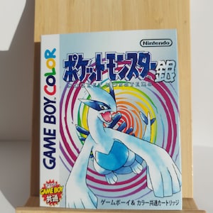May include: A Game Boy Color game cartridge for Pokemon Silver, featuring a blue and white Pokemon on a swirling rainbow background. The text on the cartridge reads "Pocket Monsters Silver" and "Nintendo".