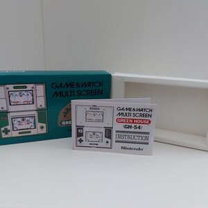 Op de afbeelding: Een turquoise blauwe doos met een Game & Watch Multi Screen Green House (GH-54) videogame erin. De doos heeft een afbeelding van het spel op de voorkant. Het spel is een draagbaar apparaat met twee schermen. Het spel zit in de originele verpakking. De doos bevat ook een handleiding.