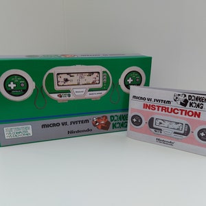 Könnte beinhalten: Eine grün-weiße Handheld-Videospielkonsole mit einer Donkey Kong 3-Spielkassette. Die Konsole befindet sich in ihrer Originalverpackung mit einer separaten Bedienungsanleitung. Die Verpackung ist grün und weiß mit dem Nintendo-Logo und dem Spieltitel.