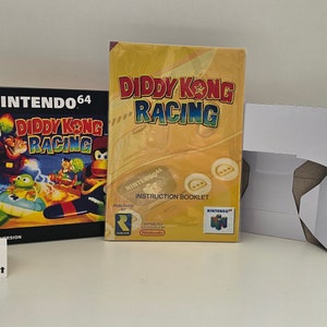 Puede incluir: Un cartucho de juego de Nintendo 64 y un folleto de instrucciones para Diddy Kong Racing. El cartucho de juego está en una caja de plástico negra con una imagen colorida de Diddy Kong y otros personajes. El folleto de instrucciones es amarillo con una imagen grande de Diddy Kong y el título del juego.