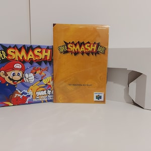 May include: A Super Smash Bros. video game box set for the Nintendo 64. The box is white with a cutout for the game cartridge. The instruction booklet is yellow with the Super Smash Bros. logo and the words "Instruction Booklet". The game case is blue with a picture of Mario on it. The text on the case reads "Super Smash" and "Duke it out as your favorite Nintendo characters."
