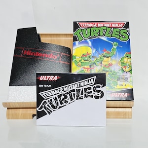 Peut inclure: Une cartouche de jeu Teenage Mutant Ninja Turtles noir et blanc pour la console Nintendo Entertainment System. La cartouche est sur un support en bois avec un boîtier de cartouche Nintendo noir derrière. La cartouche de jeu porte les mots "Teenage Mutant Ninja Turtles" et "Ultra" imprimés dessus.