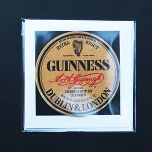 May include: A framed Guinness advertisement featuring a circular label with the Guinness logo and text. The label is brown with black and red text, including "GUINNESS" and "Dublin & London." The image is in a clear plastic sleeve.