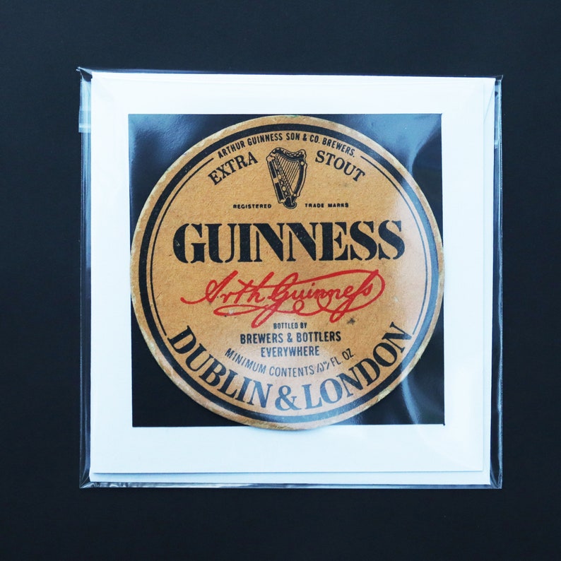 May include: A framed Guinness advertisement featuring a circular label with the Guinness logo and text. The label is brown with black and red text, including "GUINNESS" and "Dublin & London." The image is in a clear plastic sleeve.