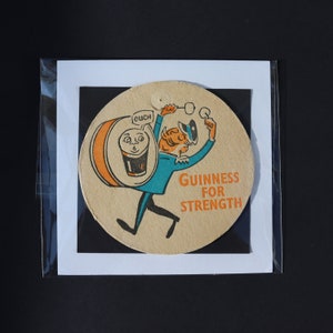 May include: A vintage Guinness beer coaster featuring a cartoon character in a blue outfit, carrying a Guinness pint. The coaster has the text "Guinness For Strength" in orange. The character is also holding two small glasses.