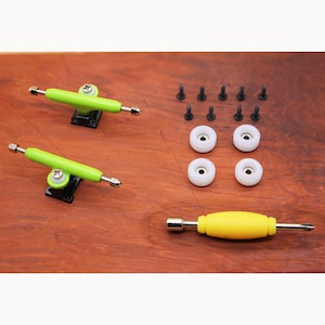 Puede incluir: Un conjunto de piezas de fingerboard que incluye dos ejes verdes, cuatro ruedas blancas, un destornillador amarillo y ocho tornillos negros.
