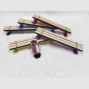 May include: A collection of miniature wooden benches with colorful supports, including red, blue, yellow, purple, and black. A small wooden finger skateboard rests near the benches. The benches have a light wood grain finish with black lines.