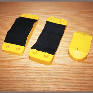 May include: Three yellow and black rectangular objects. Two are long with a black strip in the center, and the third is shorter and rounded. The objects are on a wooden surface.