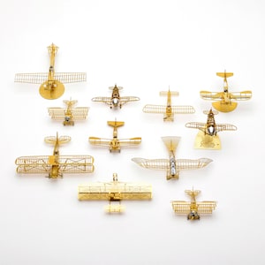 May include: A collection of 12 gold metal model airplanes, each with a unique design. The models are displayed on a white background.