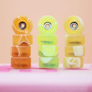 May include: Three stacks of fingerboard wheels. The first stack is orange and white, the second is yellow and white, and the third is yellow and white.