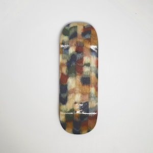 Pode incluir: Um deck de fingerboard com um padrão abstrato multicolorido e texturas semelhantes a pinceladas em tons de castanho, bege, azul escuro, verde e vermelho. O deck de madeira tem um acabamento liso e brilhante e quatro furos de montagem.